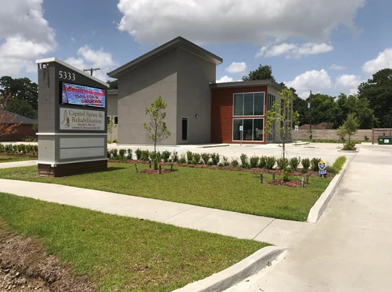 Exterior view of a healthcare facility with landscaped grounds, signage, and a parking area entrance.